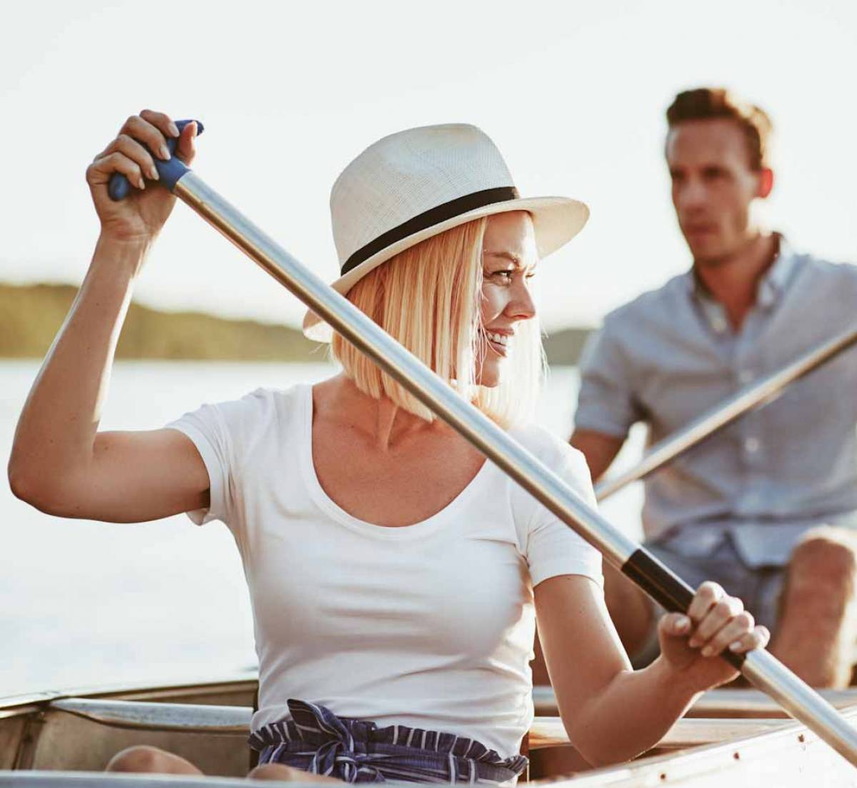 Smiling young woman paddling a canoe with her boyfriend on a lake on a sunny summer day